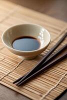 Soy sauce in a small bowl next to chopsticks placed on bamboo mat in a serene dining setting photo
