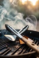 Grilling tools rest on a hot grill with smoke rising during a summer evening barbeque in the backyard photo