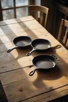 Three cast iron skillets on a rustic wooden table in warm afternoon light photo