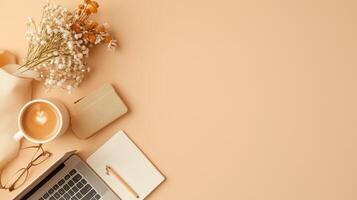 Cozy workspace featuring a laptop, coffee, notebook, and dried flowers on a pastel background photo