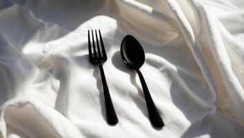 Stylish black fork and spoon on elegant white fabric with soft lighting enhancing their modern design photo