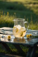 Refreshing lemonade pitcher with ice and lemon slices on a wooden table in a sunny outdoor setting photo
