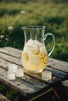 Refreshing lemonade pitcher rests on a wooden table outdoors with ice cubes and lemon slices under the bright sun photo