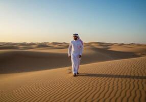 a Saudi Gulf Arab man wearing a ghutra and a bisht walking in the desert and looking at something, the concept of love of the homeland and belonging to it, photo