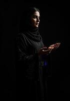 Woman in Hijab Praying with Open Hands Against Dark Background photo