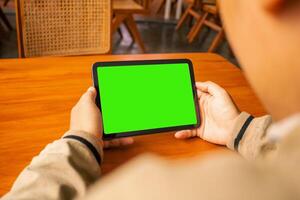 Man viewing a tablet with a blank green screen in a cozy cafe setting, perfect for design templates. photo
