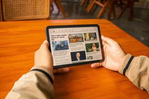 March 08, 2025, semarang, indonesia, Hands holding a tablet displaying an online news website with global headlines. photo