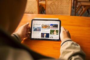 March 08, 2025, semarang, indonesia, Person reading news on a tablet while sitting at a wooden table in a cozy setting. photo