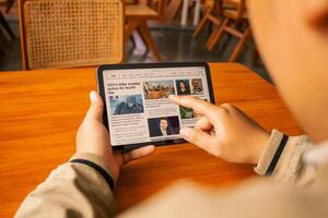 March 8, 2025, Semarang, Indonesia, a person is reading the news using an iPad on a cafe table. photo