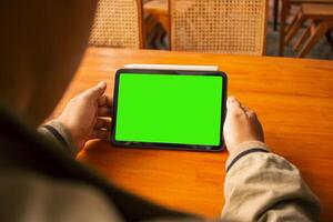 Close-up of hands using a tablet with a green screen, ideal for mockups or digital presentations. photo