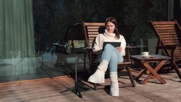 Young professional working remotely on tablet while conferencing from wooden terrace during sunny winter day, using smartphone on tripod video