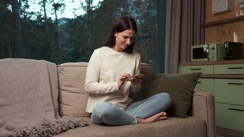 Comfortable woman sitting on a sofa in her modern apartment, browsing social media on her smartphone and smiling, enjoying a relaxing evening video
