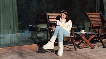 Young woman enjoys working on a tablet while drinking coffee on a sunny winter balcony, taking advantage of the beautiful weather and mountain view video