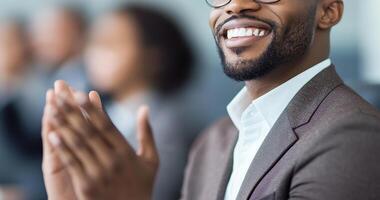 smiling man in suit claps his hands, showcasing positive atmosphere in professional setting. His expression reflects enthusiasm and engagement during meeting or presentation photo