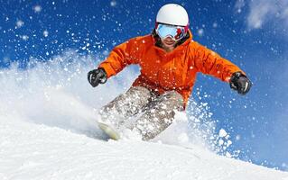 snowboarder in orange jacket carving through fresh powder snow against clear blue sky, showcasing dynamic movement and excitement photo