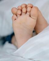 The feet of a small child in a parent's bed on white sheets rolled in a white blanket photo