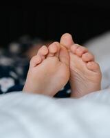 The feet of a small child in a parent's bed on white sheets rolled in a white blanket photo