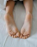 The feet of a small child in a parent's bed on white sheets rolled in a white blanket photo