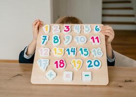 the boy learns to count, holds a board with numbers-puzzles arranged in order from 1 to 20 photo