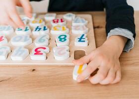 boy learns to count by laying out numbers from 1 to 20 on the board, boy 4-5 years old European appearance, at home in the living room sitting at the table, preparation for school photo