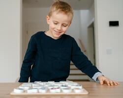 boy learns to count by laying out numbers from 1 to 20 on the board, boy 4-5 years old European appearance, at home in the living room sitting at the table, preparation for school photo