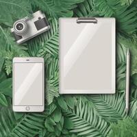 Creative workspace layout with camera, smartphone, clipboard, and pen on leafy background photo