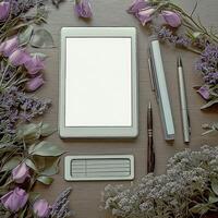 Elegant workspace setup with blank tablet and stationery surrounded by flowers photo