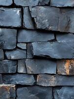 Close-up of a rough, grey stacked stone wall, background is out-of-focus photo