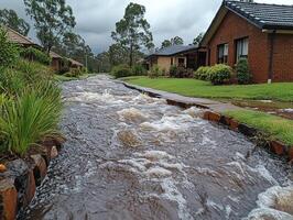 Suburban street flooding, rapid water flow in drainage ditch, houses, cloudy sky photo
