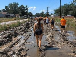 Volunteers wade through muddy street, post-disaster cleanup in residential area photo