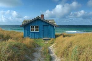 Blue wooden house sits on beach sand, with sea and cloudy sky. For travel use photo