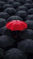 Red umbrella standing out from crowd of black umbrellas symbolizing uniqueness and individuality photo
