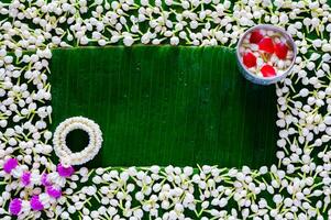 Flowers in water bowl for blessing with garland on empty space of wet banana leaf and jasmine background for Thailand Songkran festival background. photo