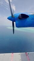 view from the water airplane window to the rotating propellers of the engine of a local airlines plane flying over the islands of Maldives, blue sky video
