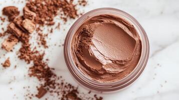 Creamy chocolate dessert in a jar with scattered cocoa powder on a marble background showcasing delectable texture and color photo