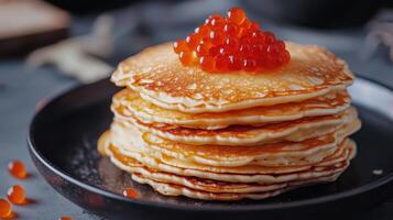 Stack of golden pancakes topped with vibrant fish roe served on a black plate in a modern kitchen setting during breakfast time photo