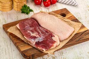 Two raw meat pieces on a cutting board with a knife and spices photo