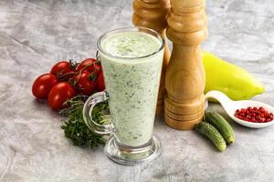 A glass of green smoothie next to a pepper and a tomato photo