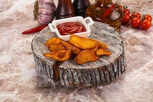 A wooden plate with some chips and ketchup photo