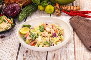 A bowl of salad with vegetables and a napkin on a table photo