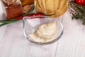 A bowl of dressing sitting on a table next to a bowl of tomatoes photo
