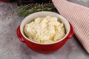 A bowl of butter sits on a table next to a spoon photo
