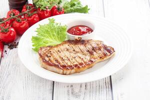 Grilled pork steak with tomato sauce and lettuce on a white plate photo