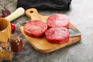 Three raw beef steaks on a cutting board with spices and other ingredients photo