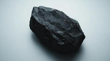 Large black rock displayed on a light background showcases texture and surface detail under soft lighting conditions photo