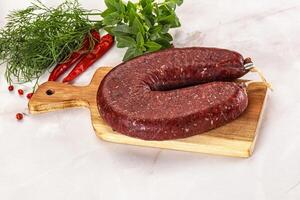 A large raw sausage on a cutting board with herbs photo