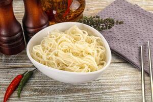 A bowl of noodles with chopsticks and bottles of sauce photo