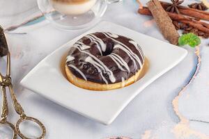 A chocolate donut on a white plate with a cup of coffee photo