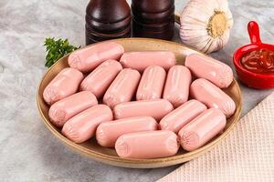 A bowl of sausages on a table next to a bottle of ketchup photo