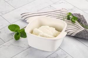 A bowl of yogurt sits on a counter next to a towel photo